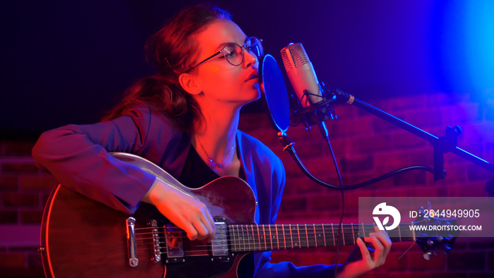 A young woman playing guitar and singing in neon lighting