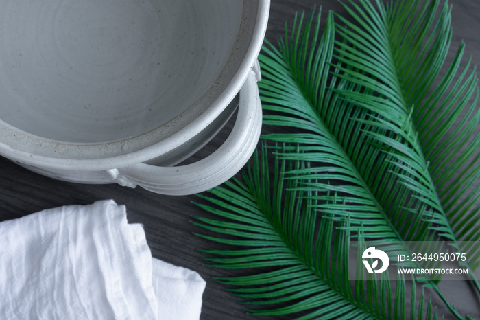 Close up of clay pot of water with white linen and palm branch on a dark wood background