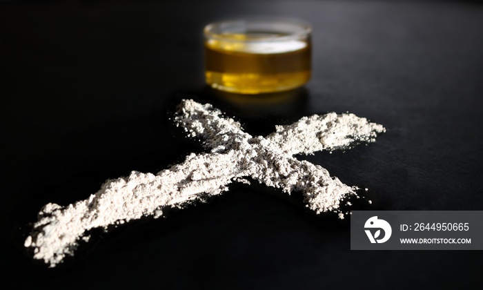 Side view of ashes made from burned palm crosses beside glass containing olive oil for use on Ash Wednesday