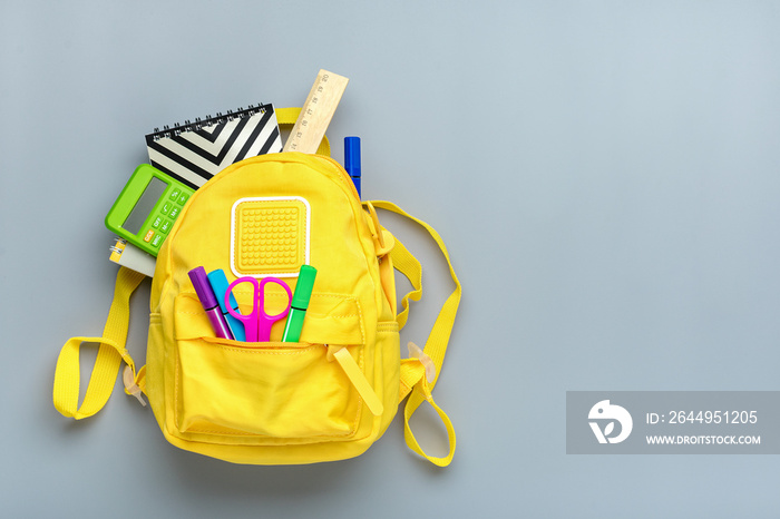 Back to school, education concept. Yellow backpack with school supplies - notebook, pens, ruler, calculator, scissors isolated on gray background. Top view. Copy space Flat lay composition Banner