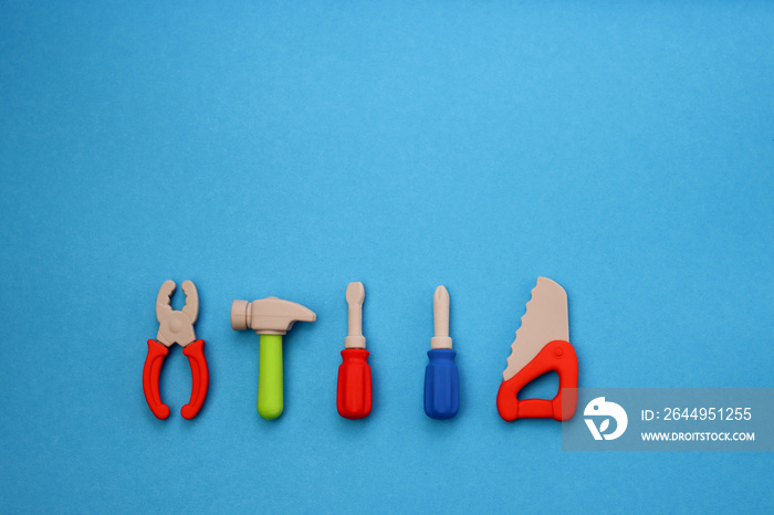 Children’s mini versions of screwdrivers, saws, hammer and pliers on a blue background. Children’s toolset