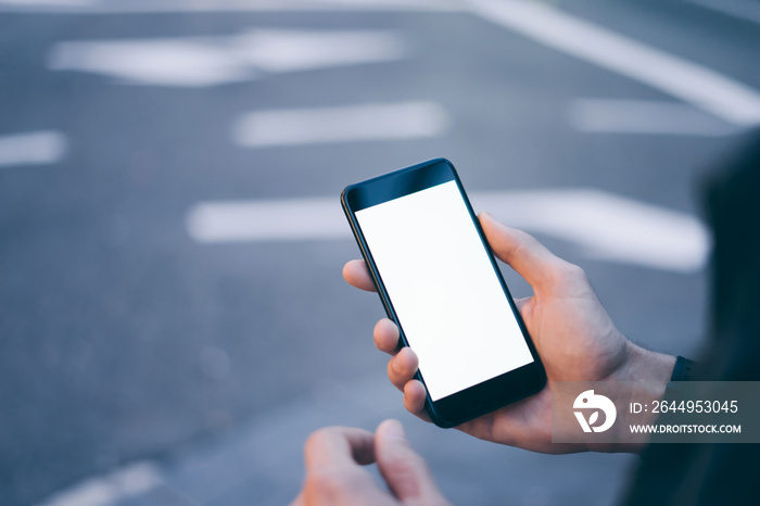 Closeup image of male hand holding smartphone with blank screen. Mockup ready for text message or content. Man’s hands with cellphone. Empty display. Night street, bokeh light