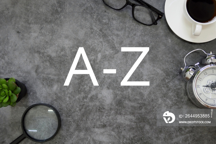 Top view of sunglasses,a cup of coffee, clock,plant, and magnifying glass on grey floor background written with A-Z.