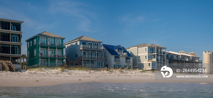 Beach houses and apartments at Destin, Florida beach. White sand shore with dunes at the front of the houses against the blue sky background.