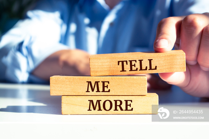 Close up on businessman holding a wooden block with  TELL ME MORE  message