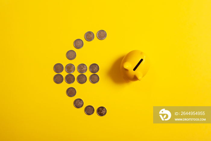 Top view of euro symbol made from euro coins with piggy bank beside it and yellow background