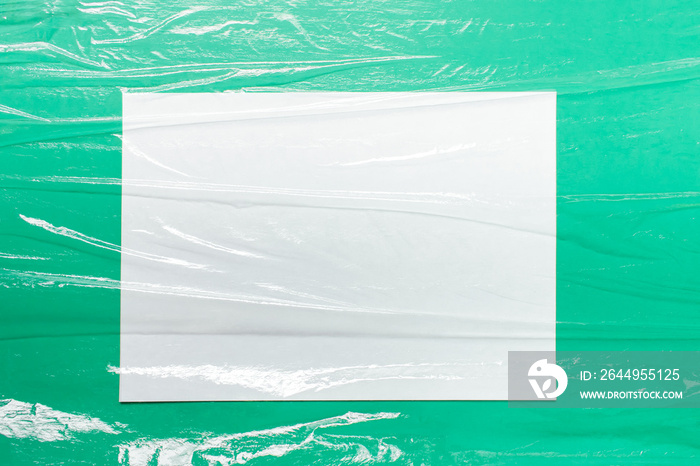 Mockup template with A4 paper sheet and folded uneven celofan food film foil on green paper background.