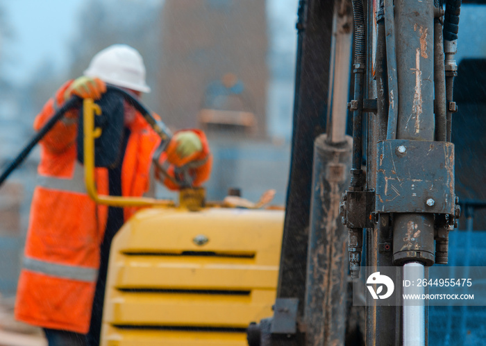 Construction worker in safety gloovs filling excavator with red diesel fuel on construction site