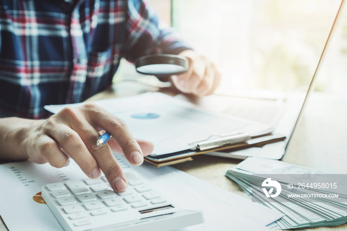 The accountant is pressing the calculator to calculating check the accuracy of the investment budget with using computer laptop and document data to analysis.