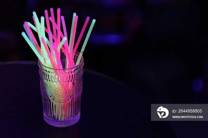 close up glass of colorful light sticks in dark