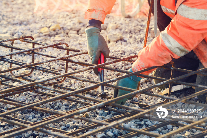 Builder’s hands fixing steel reinforcement bars at construction site. Steel fixer assembling reinforcement cage. Selective focus