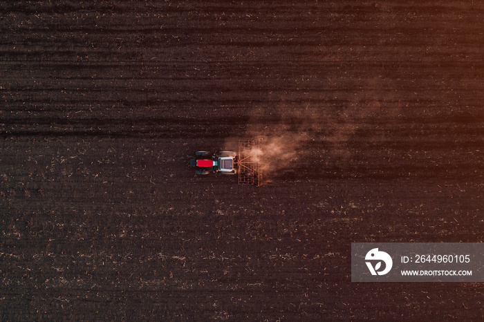 Agricultural tractor with tiller attached performing soil tillage in field, aerial view