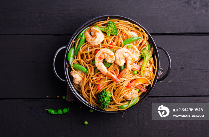 Stir-fried spaghetti or stir-fry noodles with vegetables and shrimp in a black bowl. dark background, top view