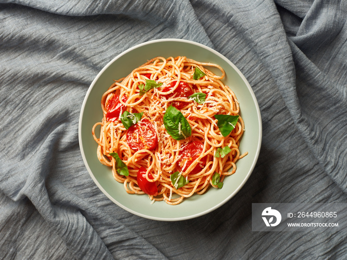 Plate of spaghetti with cherry tomatoes and fresh basil on tablecloth top view