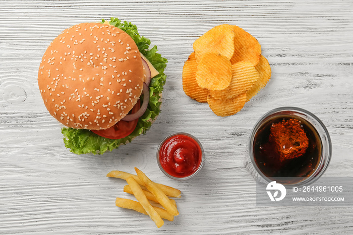 Tasty cheeseburger with snack and coke on wooden table