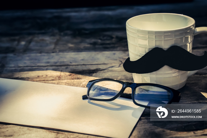 Happy fathers day concept. coffee cup with black paper mustache, heart tag with Happy father’s day text and newspaper, glasses on wooden table background.