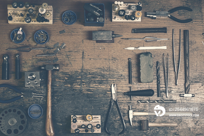 Top view of different goldsmiths tools on the jewelry workplace. Desktop for craft jewelry making with professional tools. Aerial view of tools over rustic wooden background. Postcard design