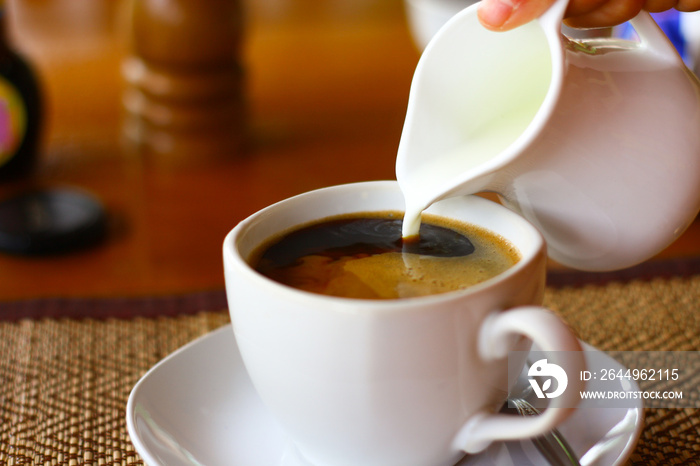 hand pouring milk to coffee cup on wood table background