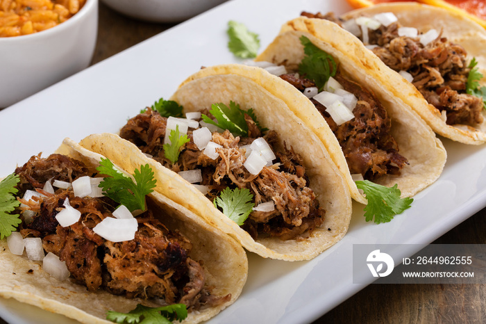 Pork carnitas tacos on corn tortillas with rice and beans