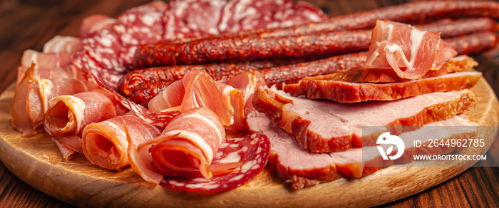 Assorted meat snacks on a wooden cutting board. Sausage, ham, bacon, smoked meats. Stock photo of meat products with blank space.