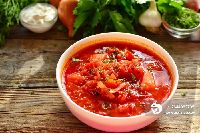 Ukrainian and Russian cuisine, red borsch. Tomato soup. Vegetable borscht made from tomato, bell pepper, parsley, onions, potatoes, carrots, cabbage and beets. Food on a wooden background.