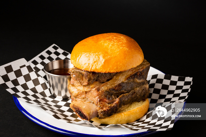 Beef rib burger on a white plate over a black background