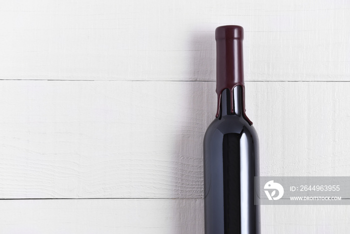 Single Bottle of Wine on a White Wood Table. The thin bottle has a wax seal over the top.