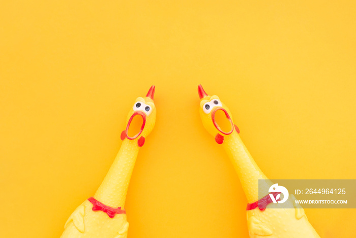 Two screaming chicken toys are isolated on a yellow background, screaming with a mouth open looking into the camera. Chicken toy on a yellow background, pattern for design.