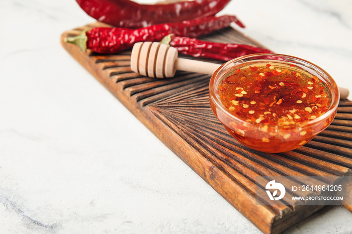 Board with hot honey and dry chili peppers on light background