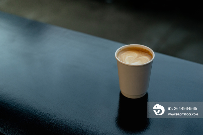 A hot latte coffee served in a paper cup on a black table at a coffee shop.