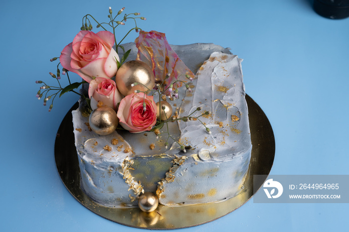 cake on a golden tray on a blue table, decorated with roses and flowers,