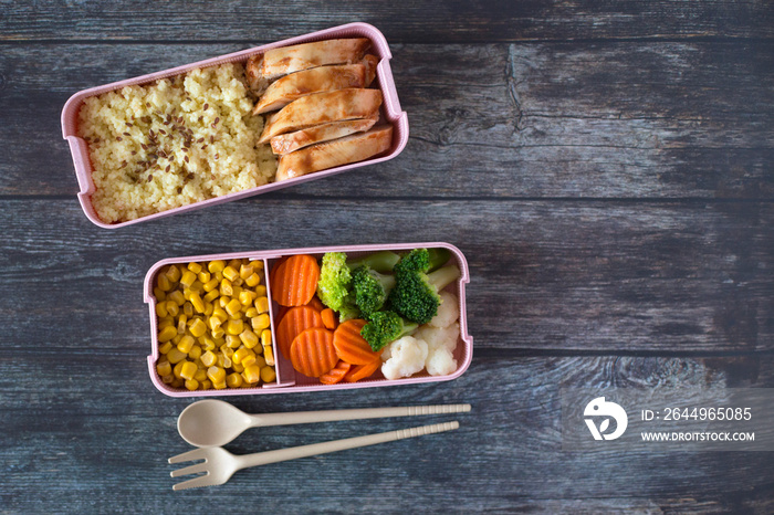 Lunch box with fresh meal on a dark wood background. Broccoli, corn, cabbage, carrots, chicken. Healthy food at work concept