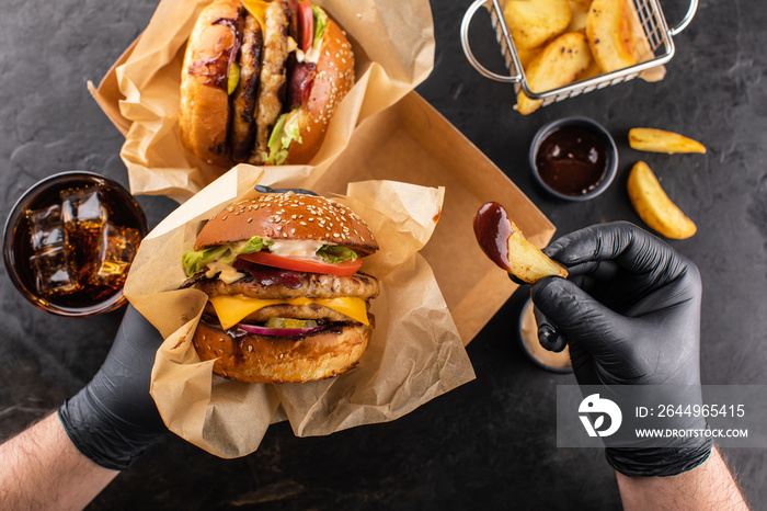 Yummy grilled chicken hamburger with double cutlet and fries in hands ready to eat. Burger and French fries top view.