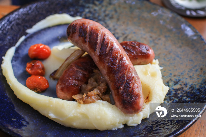 Sausages and mashed potato and gravy on black plate. Italian food concept.