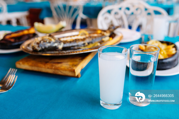 Turkish or Greek restaurant table and food dinner cuisine culture from top view. Traditional Greek ouzo or turkish raki with grilled or fried fish and appetizers on dinner table at restaurant.