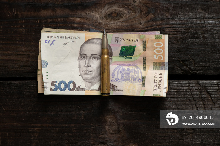 A bullet and Ukrainian hryvnia money lie on a wooden table, money for soldiers’ military weapons, the war in Ukraine