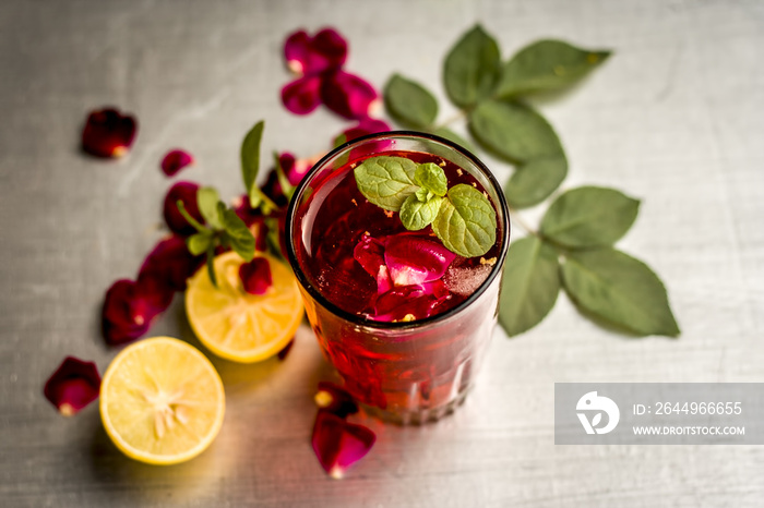 Popular Indian/Asian sharbat i.e GULAB KA SHARBAT with sliced lemon,Citrus × limon,Rosa,rose petals and mint leaves on a silver wooden surface.
