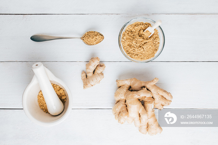 Natural ginger, ginger powder, mortar with chopped ginger and a spoon on the table