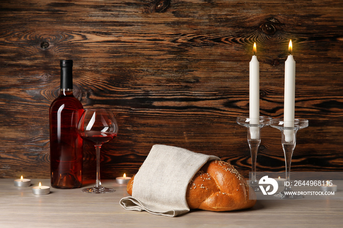 Traditional challah bread with wine and glowing candles on wooden background. Shabbat Shalom