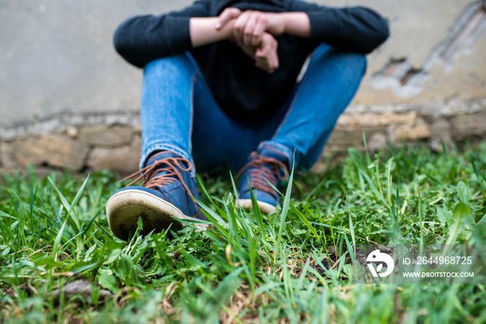 Frustrated teenage boy sitting near a crumbling wall at the correctional institute, focus on the boys shoe.