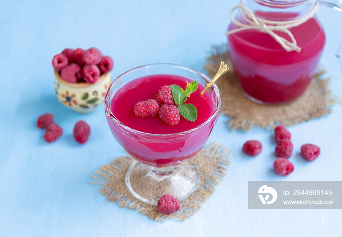 Raspberry dessert in a glass. Traditional Russian thick berry drink or jelly dessert kissel made from fresh berries, water and corn starch. Glass of cold raspberry cocktail with fresh berries and jug