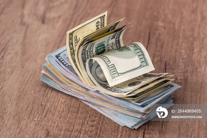 Stack of US dollars in cash in wooden desk.