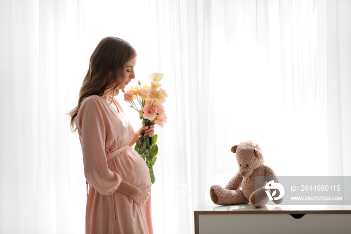 Beautiful pregnant woman with flowers near window