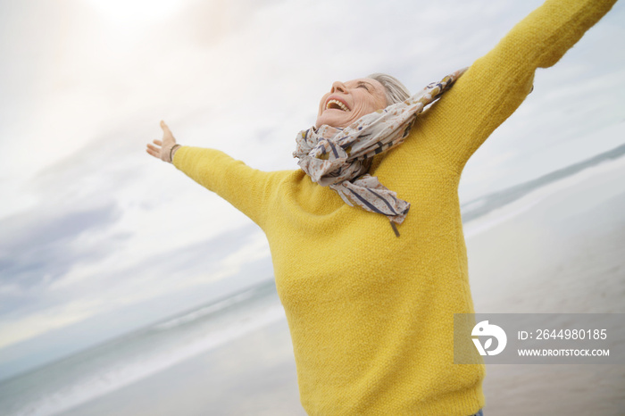 Carefree energetic senior woman playing around on beach in fall