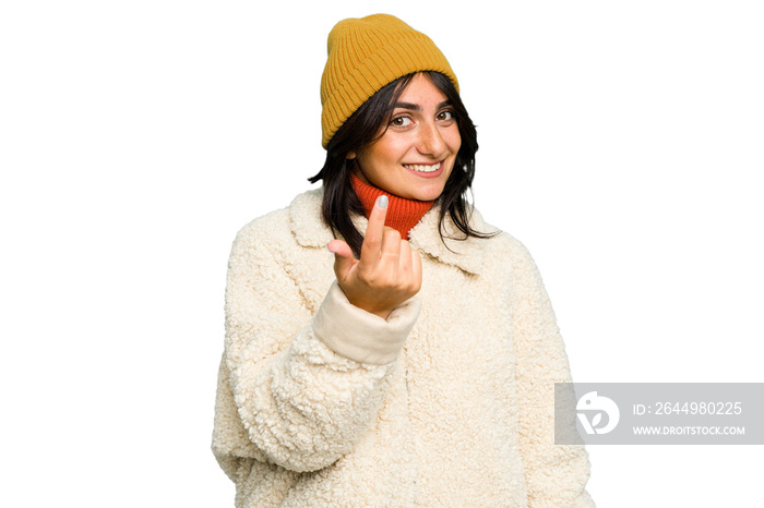 Young Indian woman wearing winter jacket and a wool cap isolated pointing with finger at you as if inviting come closer.