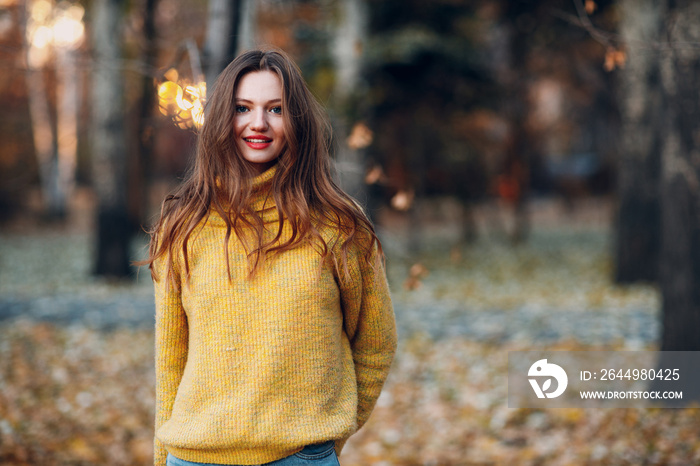 Young woman model in autumn park with yellow foliage maple leaves. Fall season fashion