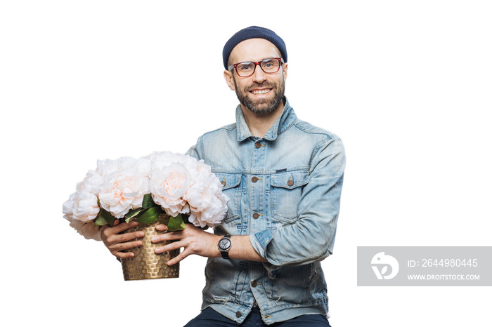 Happy delighted male buys bouquet of flowers for special occasion, wears denim jacket and denim shirt, isolated over white background. Joyful emotional man with present. Beautiful flowers for you