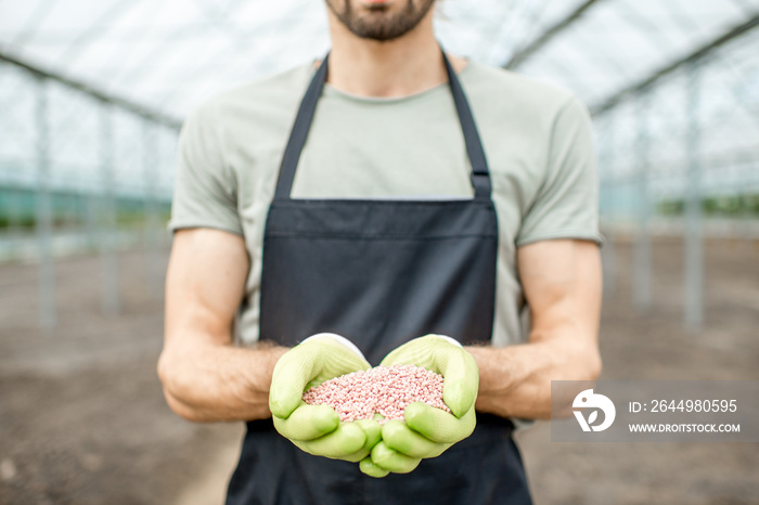 Farmer holding mineral fertilizers in the glasshouse with cultivated soil ready for fertilization