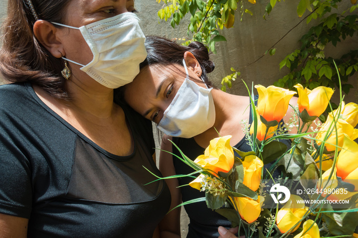 Mother and daughter mourning those lost to the coronavirus, wearing face masks, showing mutual support, hugging