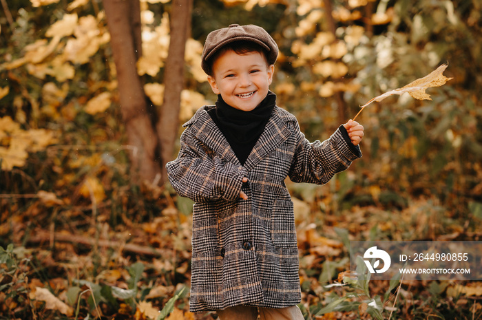 A happy baby boy is playing with a yellow maple leaf in the autumn season in the park.